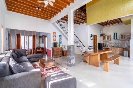 Spacious open-plan living room with wooden beamed ceiling, gray L-shaped sofa, wooden dining table, and modern kitchen in a tropical-style home. - Bali Villas